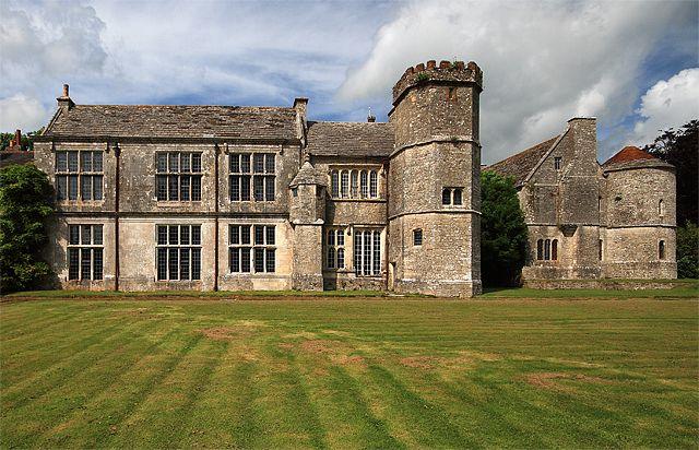 The south side of Wolfeton House near Dorchester, a medieval and Elizabethan mansion with tall lead paned windows, a pitched roof and a crenelated tower at one end.