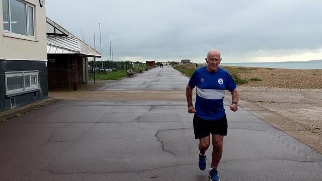 Phil Pollard running on the street on a cloudy day. He is wearing a dark blue shirt branded "Portsmouth Joggers". The sea could be seen behind him.