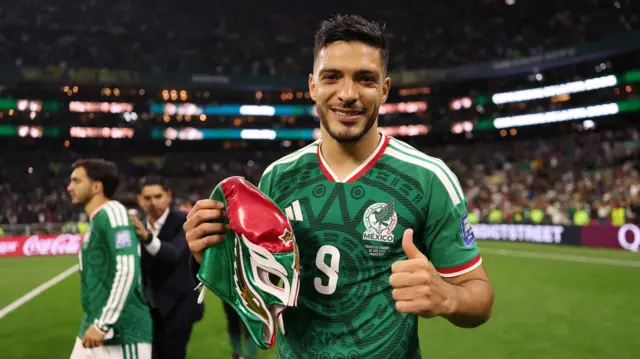 A photo of Raul Jimenez, wearing his green Mexico kit, smiling into the camera as he holds a mask and puts his thumb up after their win against Ecuador on Wednesday