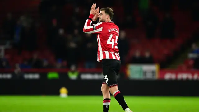A photo of Patrick Bamford facing away from the camera applauding fans in his Sheffield United home kit