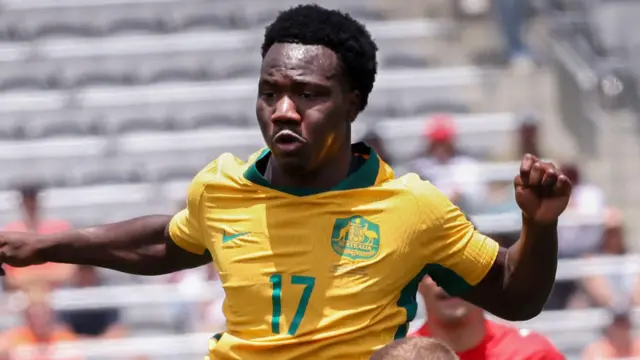Nestory Irankunda, wearing Australia's yellow home shirt with green trim, challenges for an aerial ball in a World Cup warm-up game against Switzerland