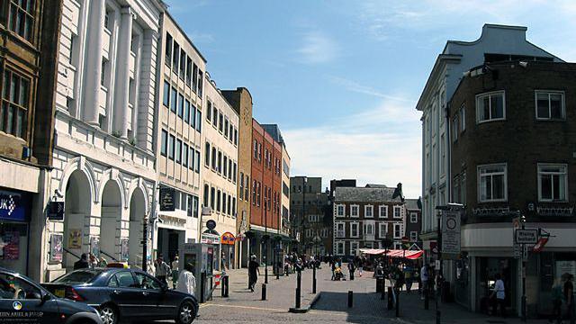 View of one side of Northampton Market Square with the Corn Exchange appearing as a white stone building with three arched entrances.