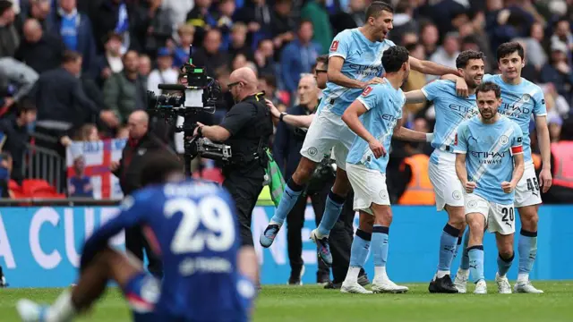 A Chelsea player sits on the turf as Man City players celebrate a goal behind him