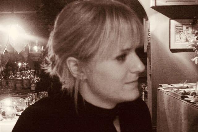 A black and white photo of a blonde woman's head and shoulders as she turns to the side in a restaurant