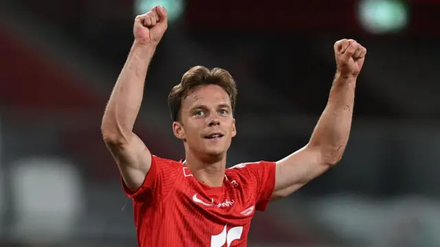 Felix Horn Myhre celebrates a win for SK Brann by putting both arms in the air. He is wearing a red shirt.
