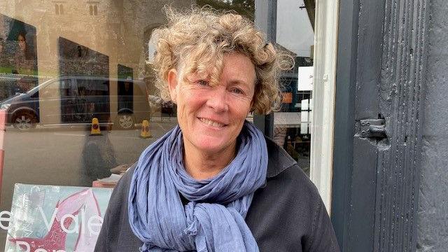 Val Harris, wearing a blue scarf and grey top, stood outside the front of The Chair gallery in Hay-on-Wye