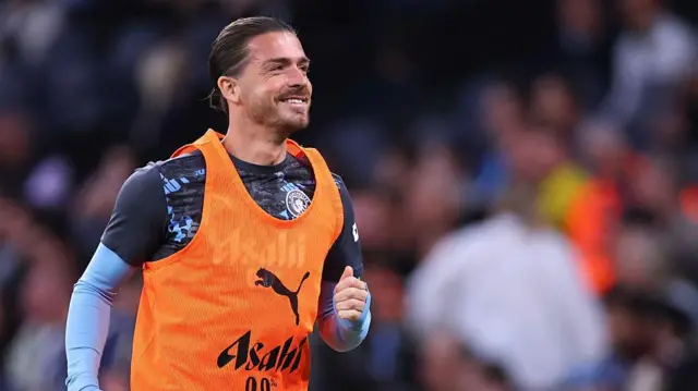 Jack Grealish warms up and smiles in an orange bib