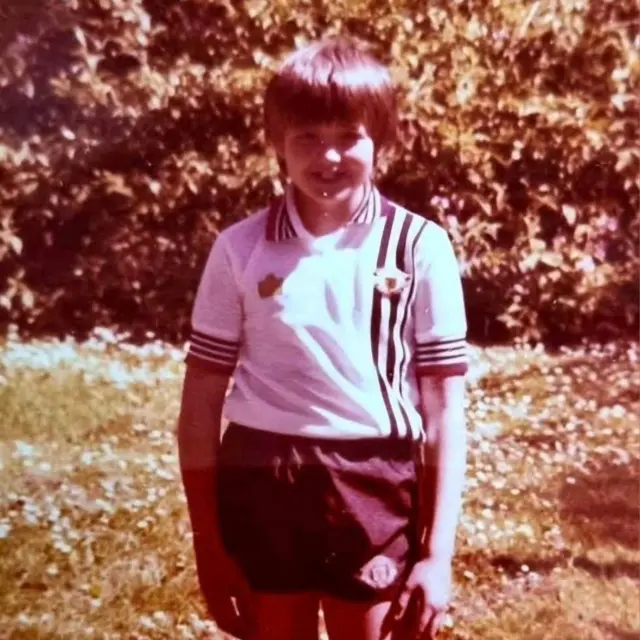 A boy in a white Manchester United shirt from the 1970s