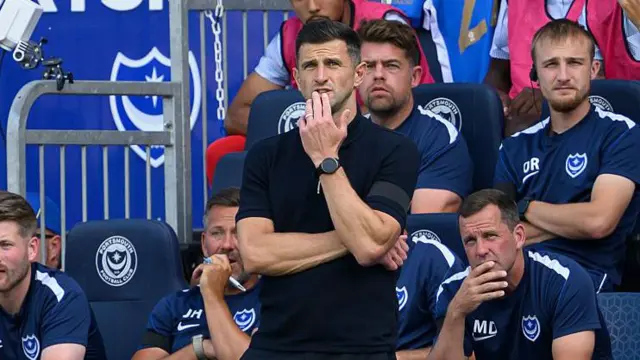 John Mousinho stands in front of the home dugout with his left hand in front of his mouth