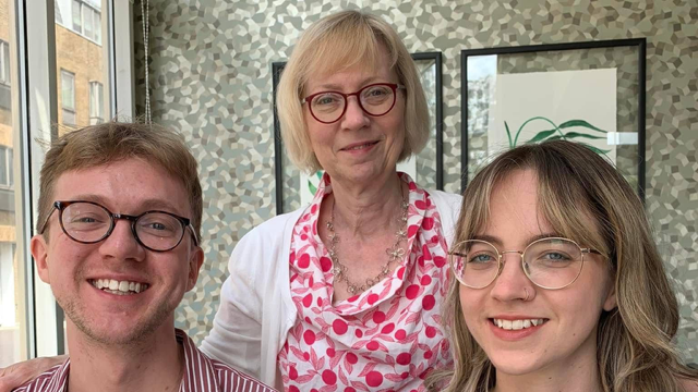 Sarah Marten standing behind her two children, who are sitting in front of her. She has her arms across their shoulders. All three are smiling, have blonde hair and wear glasses.