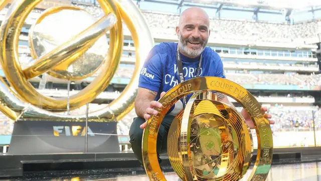 Enzo Maresca crouches down while holding the Fifa Club World Cup trophy