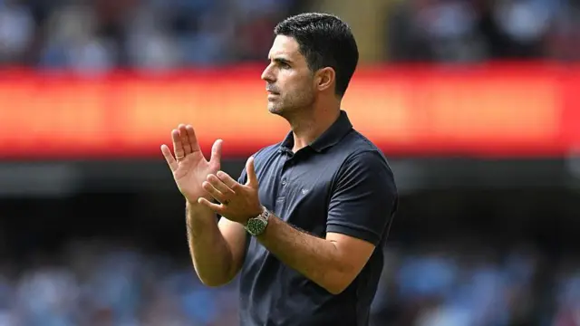 Mikel Arteta applauds wearing a dark-coloured polo shirt 