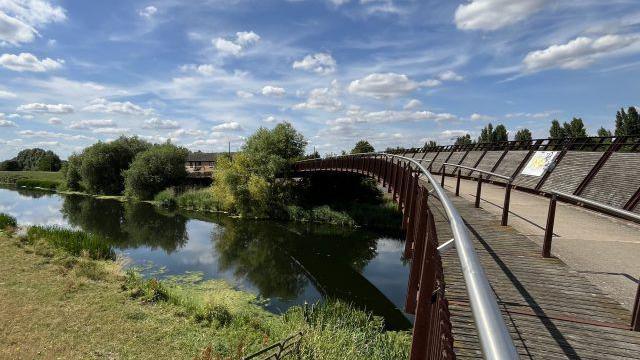 Picture of the Shanks Bridge- with metal and wooden railings - over the River Nene with trees and greenery under the bridge.