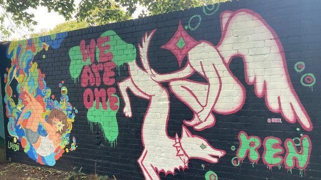 A painted black wall has text in red that says "we are one" with colourful art around it.