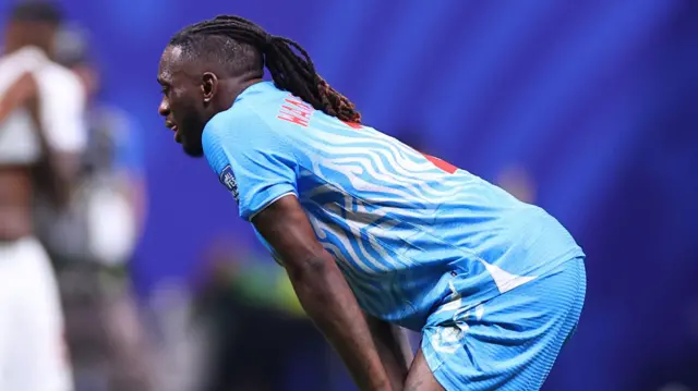 Aaron Wan-Bissaka, wearing his blue DR Congo kit, bends down with his hands on his knees with a look of dejection during their match against England on Wednesday