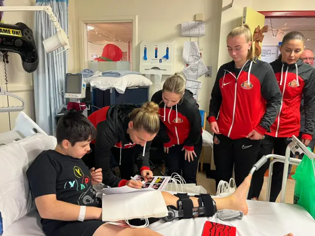 Players from Sunderland's women team with a young boy sat upright in his hospital bed