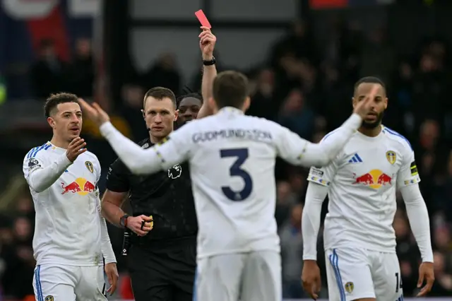 Thomas Bramall shows a red card to Leeds United's Gabriel Gudmundsson after appearing to forget he had already shown a yellow earlier in the game