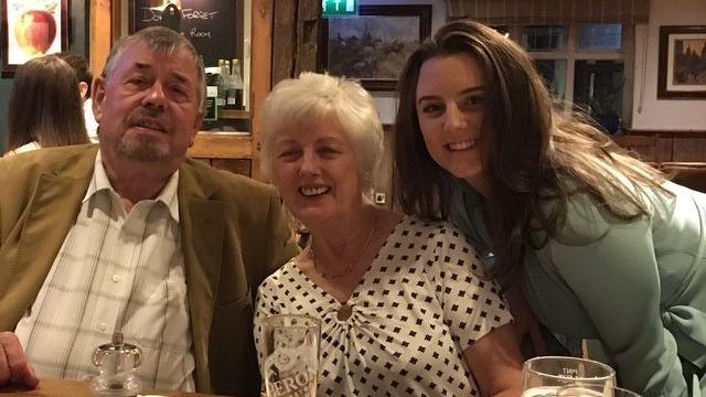 A man with grey hair , woman with white hair and younger woman with brown hair smile at the camera. They are sitting at a table in a pub.