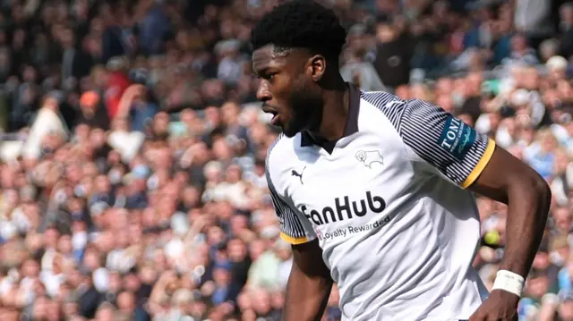 A photo of Patrick Agyemang running with the ball in a black and white Derby home kit in front of the crowd