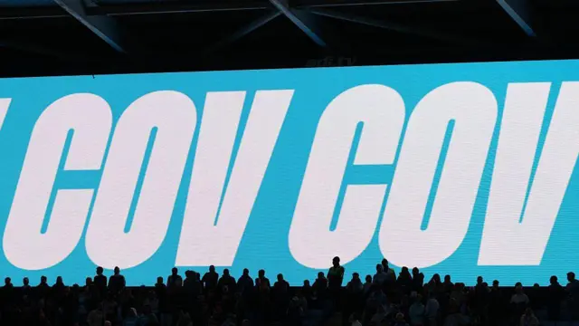 The stadium screen displays “COV, COV, COV”