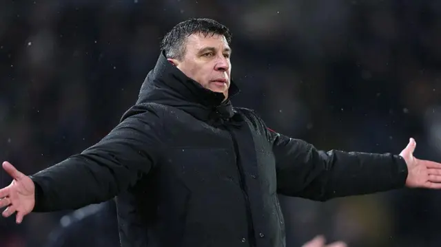 Hull City manager Sergej Jakirovic stands with arms outstretched in the rain, wearing black winter rain jacket
