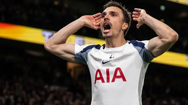 Palhinha celebrates by placing his hands close to his ears and shouting. He wears the white of Tottenham