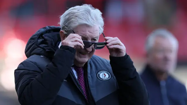 A photo of Roy Hodgson putting sunglasses on while wearing a black Bristol City jacket and a red tie
