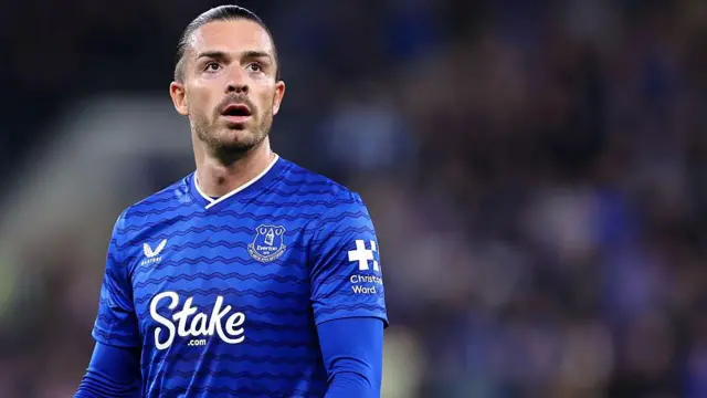 Jack Grealish, wearing Everton's blue home kit, standing still during a game