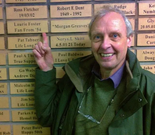 Older man smiles and points to brick with his name on