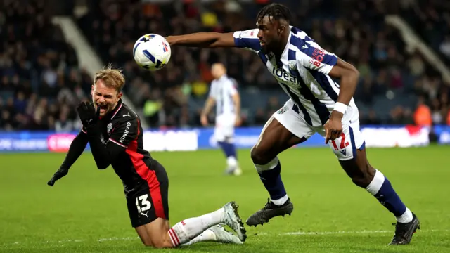 A photo of Leo Scienza falling down injured in his black and red Southampton away kit after being fouled by West Bromwich Albion player Daryl Dike