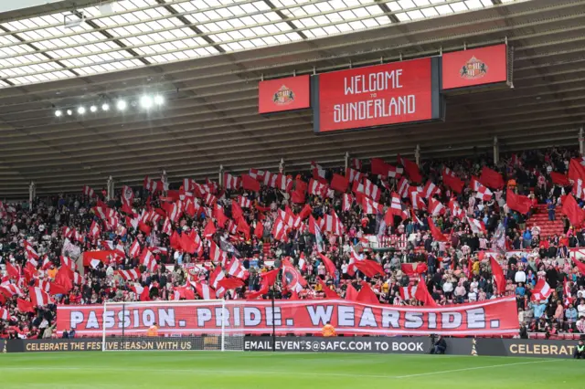 Red and white flag display at the Stadium of Light with a large banner that says 'Passion. Pride. Wearside.' 