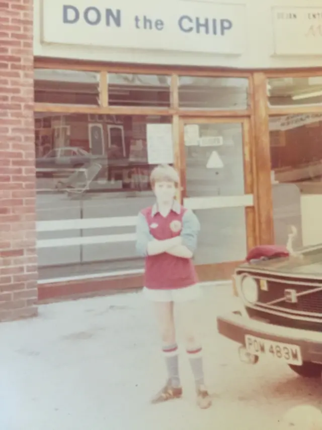 A sepia picture of a boy in full Villa kit outside a shop called Don and Chip