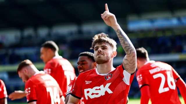 Charlie Kelman holding up one finger to the crowd to celebrate his goal with his Charlton Athletic team-mates in the background all wearing their red home kit
