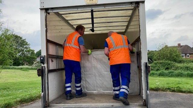 Two men loading a mattress into the back of a van