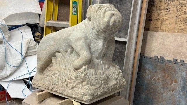 A stone sculpture of a bulldog running through reeds 