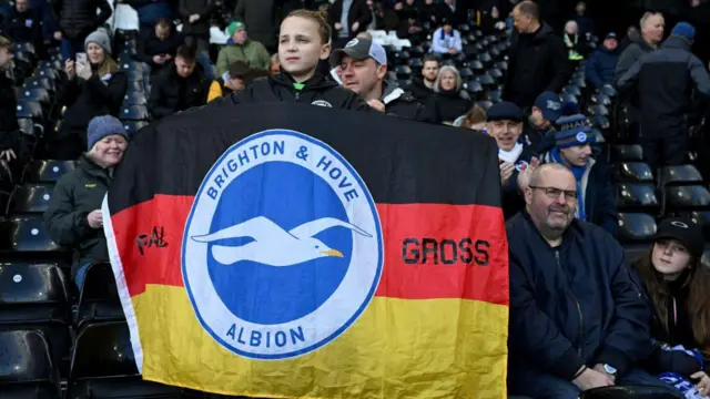 A young fan of Brighton & Hove Albion raises a flag showing support of Pascal Gross