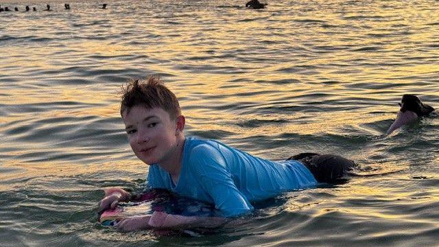 Gabrielius Misurenkovas swimming in the sea with a body board and a sunset