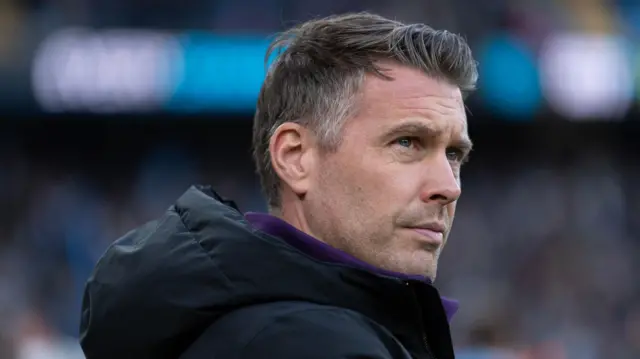 A close up of Rob Edwards, wearing a hooded black jacket, watching Wolves play Manchester City at the Etihad in January