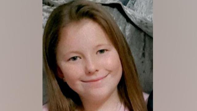 A close-up head and shoulders shot of Leah Harrison. She is smiling at the camera. She has green eyes and long brown hair.