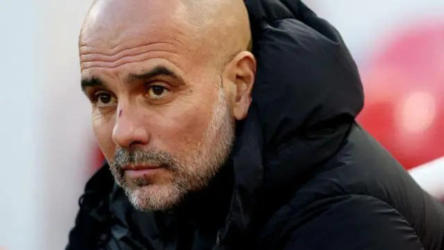 Pep Guardiola looks on wearing a black coat