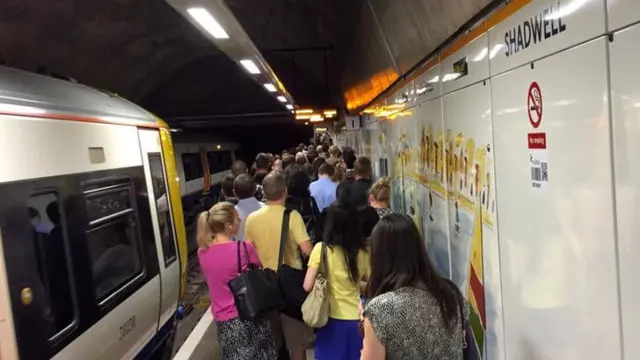 A train passes a crowded platform at Shadwell Overground Station