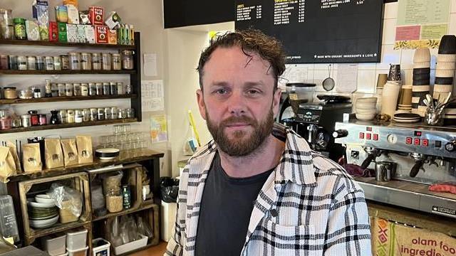 Tim Connolly from The Grain Grocer stands behind the counter with a coffee machine behind him