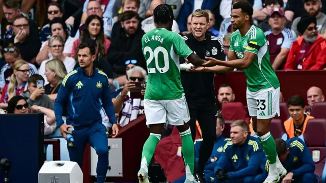 Anthony Elanga and Jacob Murphy, wearing Newcastle's green away kit, touch hands as the latter comes on for the former during the game against Aston Villa earlier this season. Eddie Howe is between the two players and home supporters can be seen in the stands in the background.