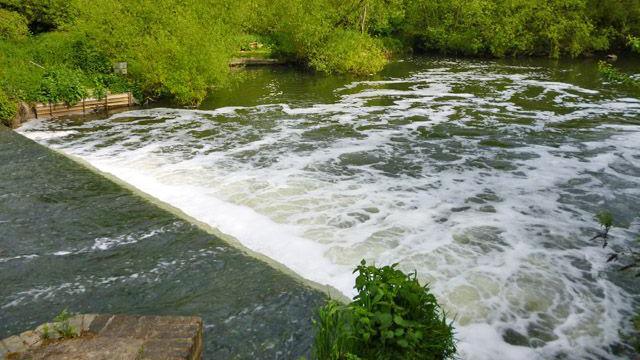 Small weir in a river surrounded by green trees.