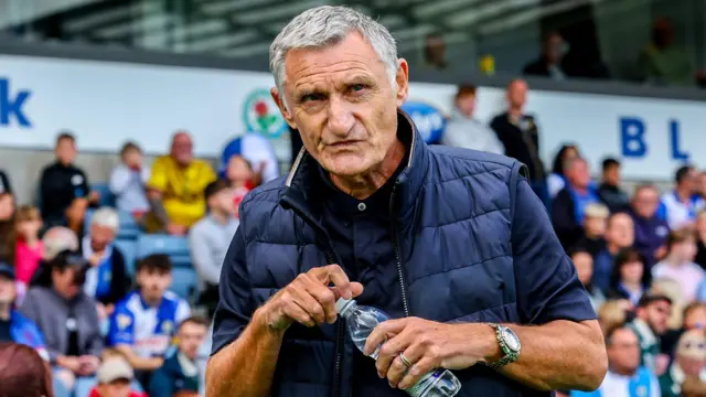 Tony Mowbray, wearing a navy blue shirt and navy blue gillet, holds a water bottle while on the touchline at Ewood Park during Blackburn's win over Middlesbrough