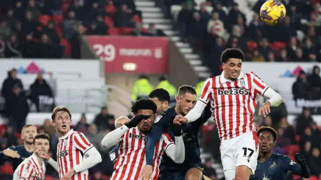 Jerry Yates of Swansea City (C) is challenged for a header by Ryan Mmaee (19) and Ki-Jana Hoever of Stoke City (17) during the Sky Bet Championship match between Stoke City and Swansea City at the bet365 Stadium on December 12, 2023 in Stoke on Trent, England.