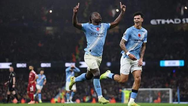 Jeremy Doku with his arms in the air celebrating his goal against Liverpool, with Nico O'Reilly smiling alongside him