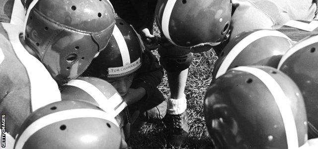 A team huddles around the quarterback in 1954