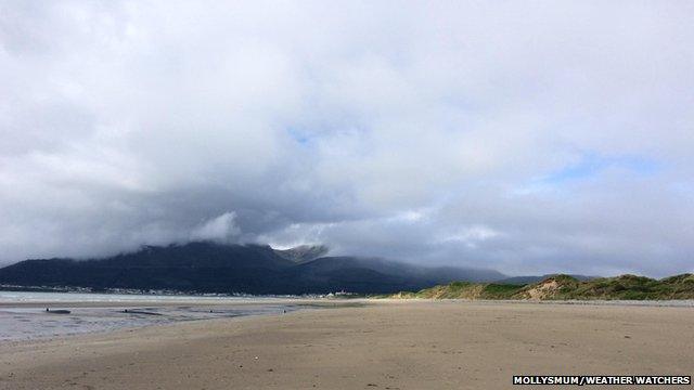 A beachfront. The sky is full of cloud and in the distance mist shrouds mountain tops