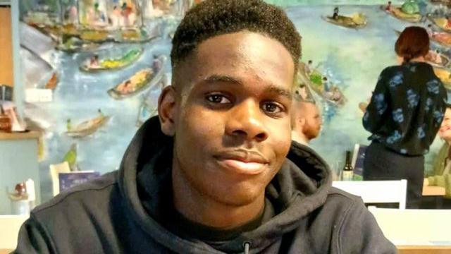Shayne Hambakachere. He has short black hair and is pictured wearing a black hoodie. He is looking directly at the camera and smiling.